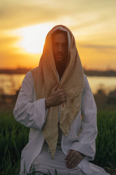 istock Jesus Christ sits in meadow in white robe at sunset. 1332138864