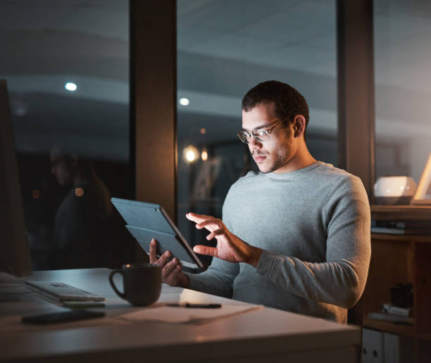 istock Shot of a young man using a digital tablet while working at night at the office 1332139195