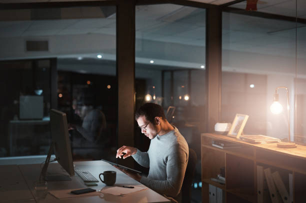 istock Shot of a young man using a digital tablet while working at night at the office 1332139201