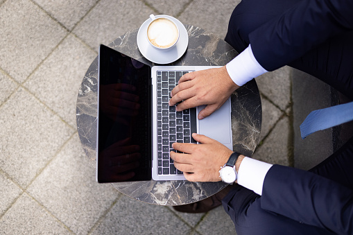 Close up aerial view of an unrecognizable middle aged successful Caucasian businessman working outside of his office using a laptop, and having a coffee cup resting next to it