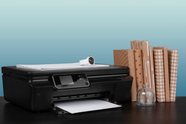 istock Compact laser printer on black desk against blue background 1332142229