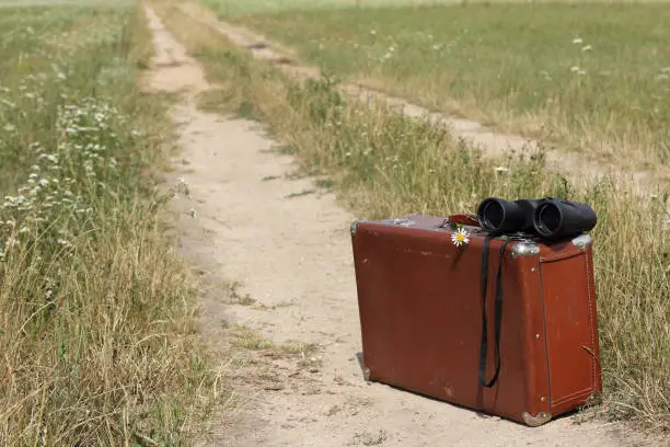 old shabby suitcase and binoculars on a field road on a summer day