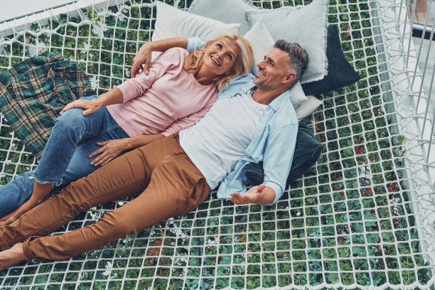 Top view of beautiful mature couple smiling and communicating Top view of beautiful mature couple smiling and communicating while relaxing in big hammock at home together mature couple stock pictures, royalty-free photos & images