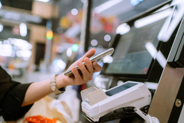 Paying with smart phone at department store. Asian woman using her mobile phone making contactless payment in supermarket. self checkout stock pictures, royalty-free photos & images