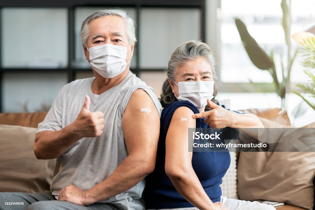 old asian senior couple wearing face mask virus protection happiness cheerful show bandage injection covid-19 vaccinated with hand gesture point and confident for virus protection Vaccination Stock Photo