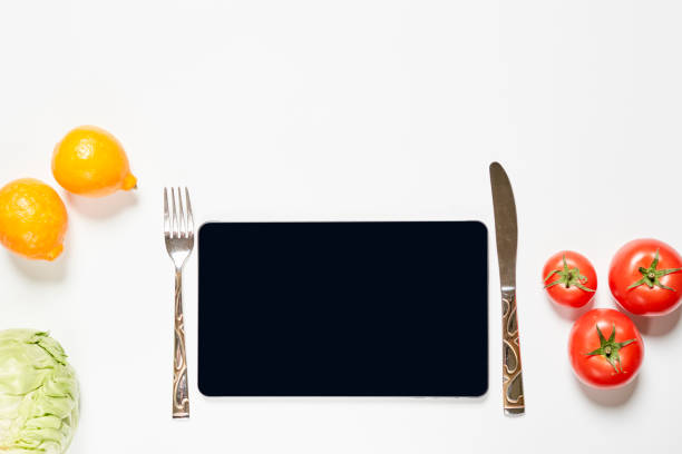 Online Delivery Service. Smartphone knife and fork on white. Fresh lemon, cabbage and tomatoes on white background