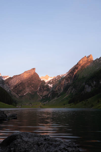 эпический восход солнца у высокогорного озера в швейцарии под названием зееальпсее. солнце светит на вершину горы на другой стороне озера.  - switzerland european alps mountain alpenglow стоковые фото и изображения