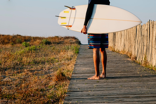 Young unrecognizable surfer holds a surfboard when the beach dawns, extreme sport, healthy and exercising.
