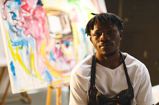Portrait of african american male painter at work looking at camera in art studio. creation and inspiration at an artists painting studio.