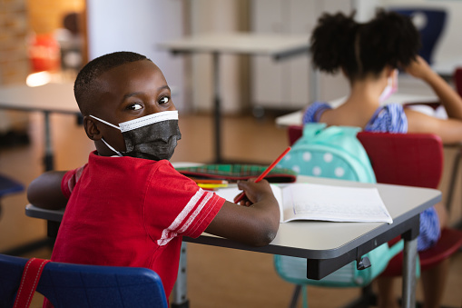 Retrato de un niño afroamericano con mascarilla sentado en su escritorio en clase en la escuela primaria photo