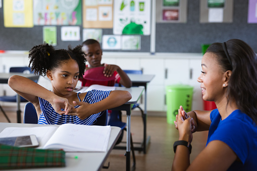 African american female teacher and a girl talking in hand sign language at elementary school. school and education concept