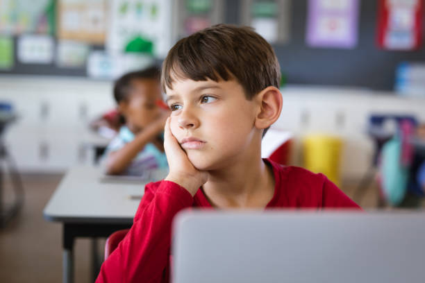 istock Sad caucasian boy with laptop sitting on his desk in the class at elementary school 1332156388