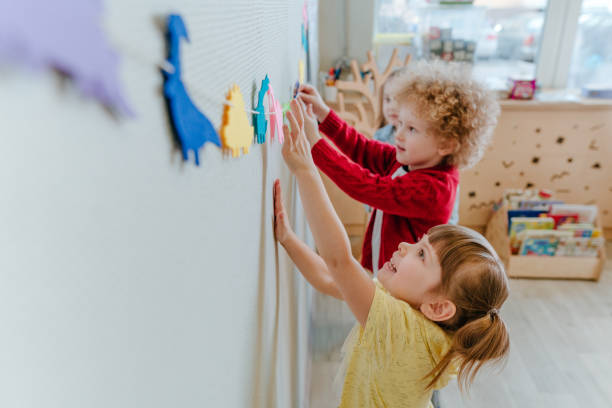 дошкольники играют в детском саду с цветными фигурками динозавров - preschool ребенок стоковые фото и изображения