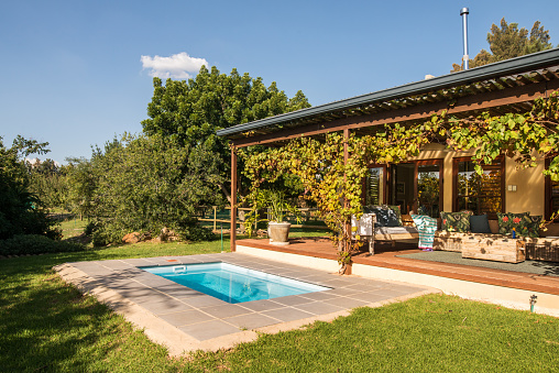 Swimming pool and backyard of a rustic home with a patio on an sunny afternoon in summer