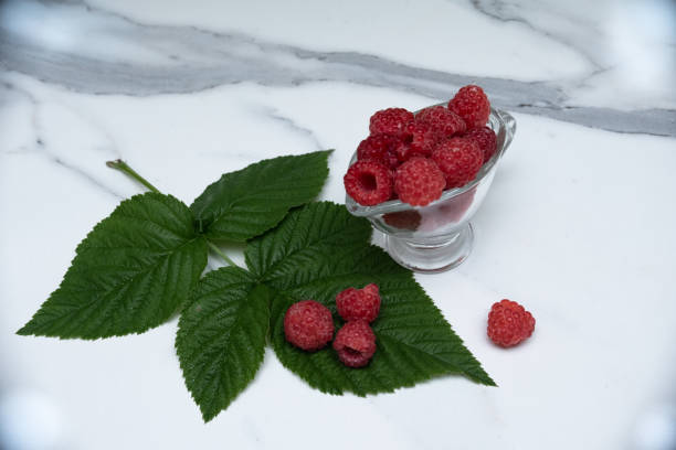 A glass cup with ripe raspberries on the kitchen table.