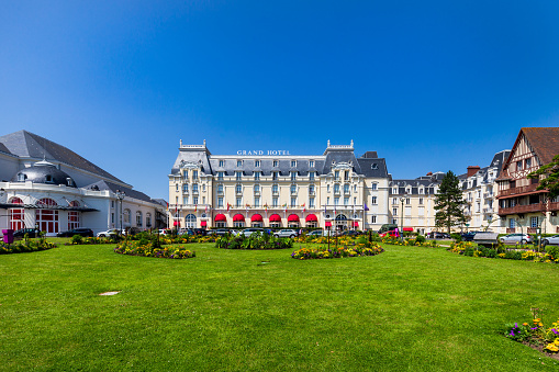 Cabourg, France - August 28, 2018: the Grand Hotel of Cabourg, where Proust used to stay, with a garden as foreground and blue sky above the building