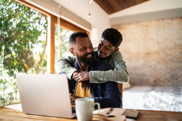 Photo of Son embracing father while he's working at home