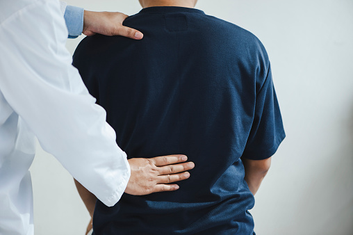 Closeup of a male Doctor or physiotherapist is doing stretching for a patient in the clinic for examining treating injured of back and Doing the Rehabilitation therapy pain
