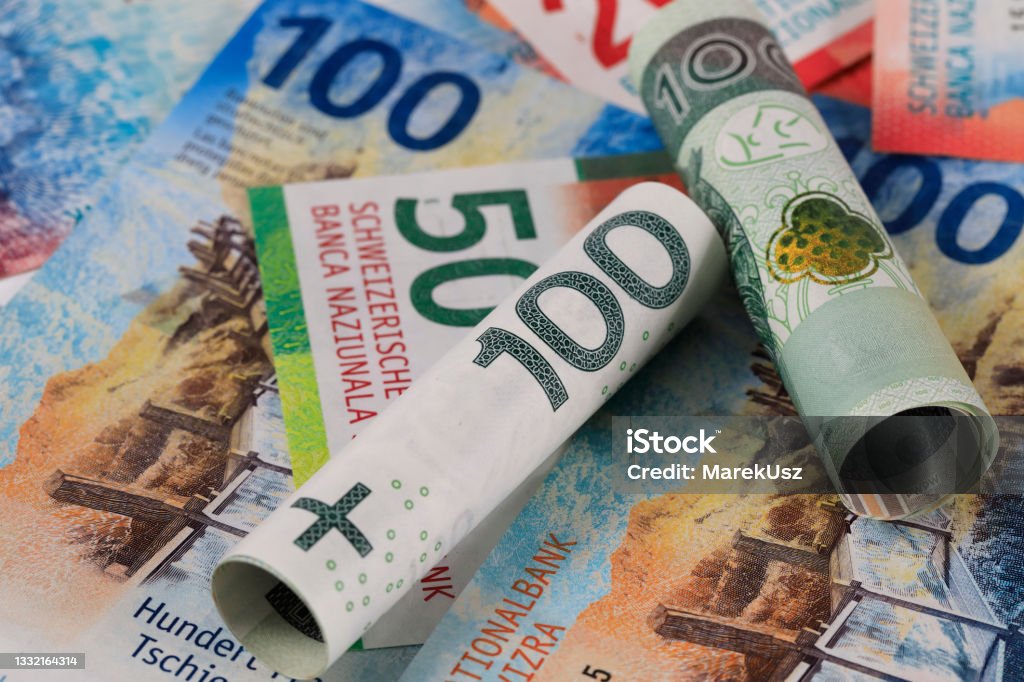 PLN and CHF currencies Rolls of Polish banknotes and non-rolled Swiss paper money express the relationship between the Swiss franc and the Polish zloty. PLN and CHF currencies. Swiss Currency Stock Photo