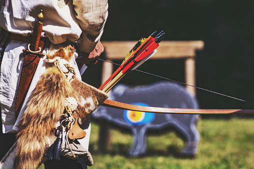 The archer is getting ready to shoot a bow and arrow at a target in the shape of a wild boar. A man in a period costume demonstrates the use of medieval weapons at an historical reenactment event.