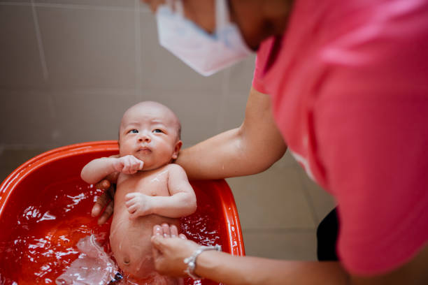 Image of an Asian grandmother taking a bath for her grandson in bathroom. Woman clean the baby's body with cloth and warm water.