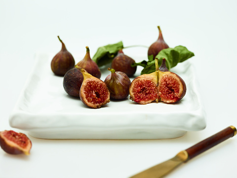 Whole figs plated on white background with fig leaves and gourmet fig and balsamic reduction pizza.