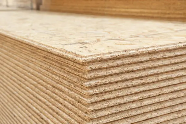 The stack of OSB sheets are stacked in a hardware store on a pallet. plywood with fragments of compressed sawdust, prepared for construction. Selective focus
