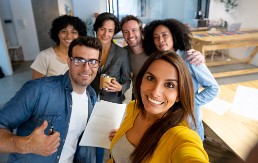 Happy group of creative Latin American people taking a selfie at the office and smiling - lifestyle at work concepts