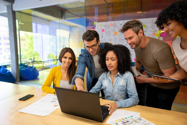 Group of designers working together in a business meeting at a creative office Group of Latin American designers working together in a business meeting at a creative office and sharing ideas while looking at a laptop computer marketing meeting stock pictures, royalty-free photos & images