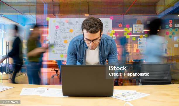 Man Working At A Creative Office Using His Computer And People Moving At The Background-foton och fler bilder på Marknadsföring