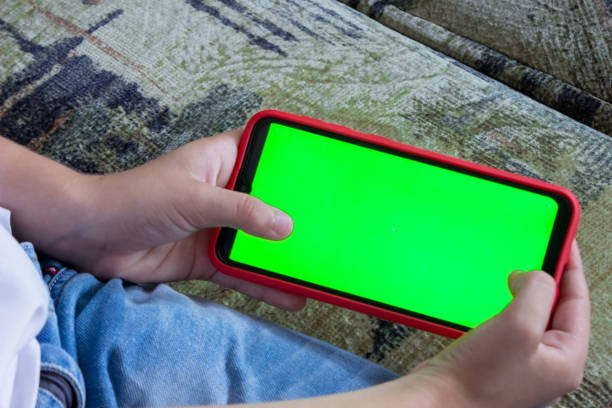 istock A child's hand holds a smartphone in a horizontal position with a green screen. Chromakey. Mock up 1332184071