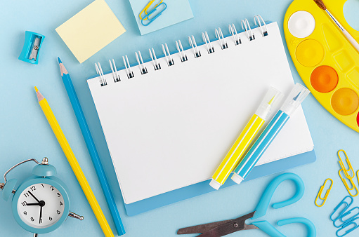 Stationery, school supplies and white blank note on pastel blue background. Top view, copy space