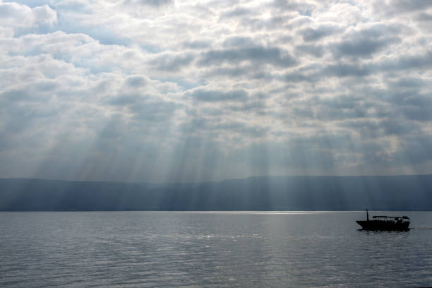 God's rays over the Sea of Galilee with boats in silhouette. God's rays over the Sea of Galilee with boats in silhouette. Many sun rays through a cloudy sky in Israel. sea of galilee stock pictures, royalty-free photos & images