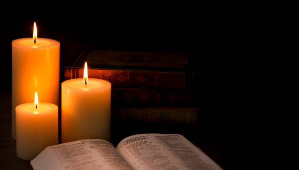 istock Three Candles Lit in a Dark Room with a Bible 1332205260