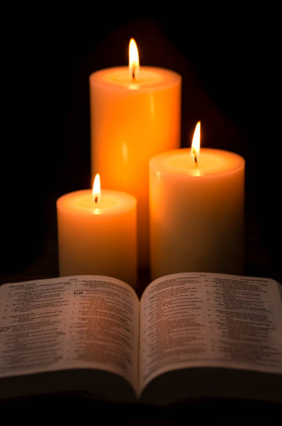 istock Three Candles Lit in a Dark Room with a Bible 1332205266