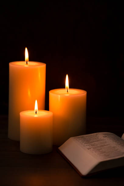 istock Three Candles Lit in a Dark Room with a Bible 1332205353