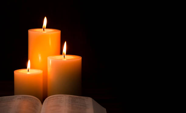 istock Three Candles Lit in a Dark Room with a Bible 1332205389