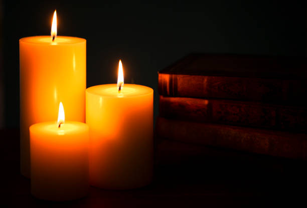 Three Pillar Candles Lit in a Dark Room with a Stack of Antique Books
