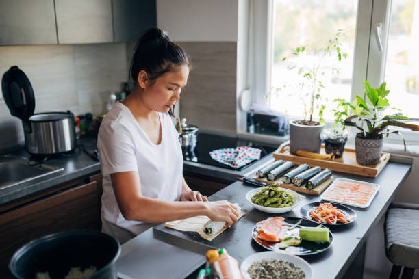 istock Woman Thai ethnicity for the lunch in her kitchen, making inside-out sushi rolls 1332208084