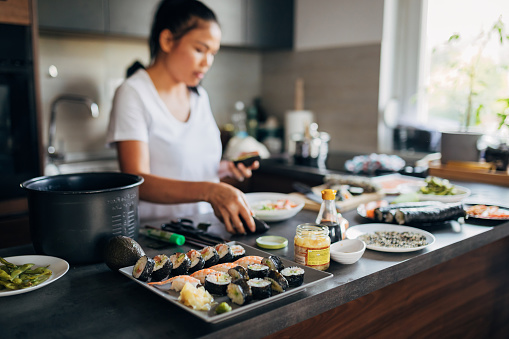 In her modern domestic kitchen, skilled Thai woman, arranging the inside out sushi rolls and Nigiri on the plate, proud of how all of them turned out