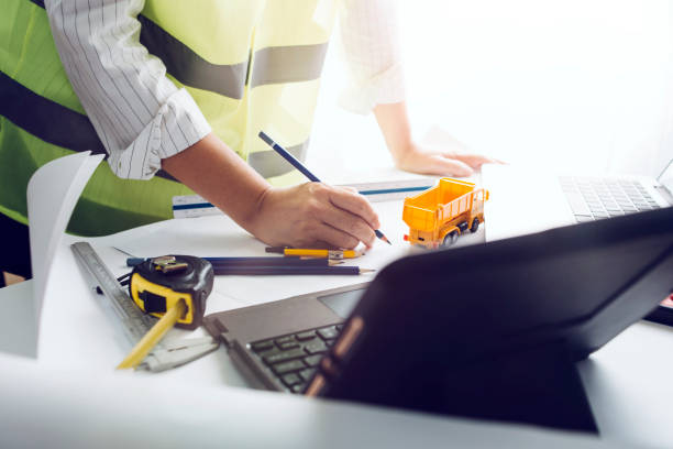 istock Two colleagues discussing data working and tablet, laptop with on on architectural project at construction site at desk in office 1332209181