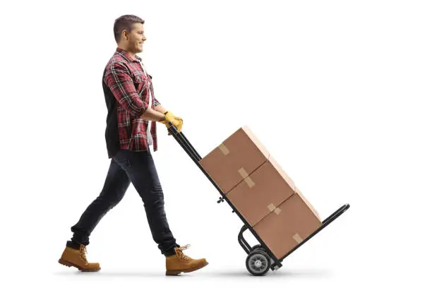 Photo of Full length profile shot of a man pushing a hand truck with cardboard boxes
