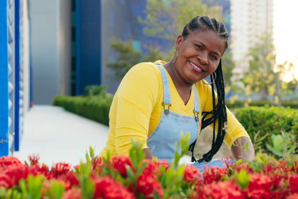 dojrzała afrykańska kobieta pozująca w pobliżu czerwonych kwiatów na świeżym powietrzu - hector zdjęcia i obrazy z banku zdjęć