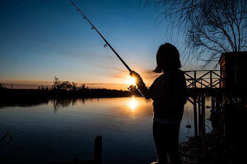 girl fishing standing on wooden pier by the river in the afternoon