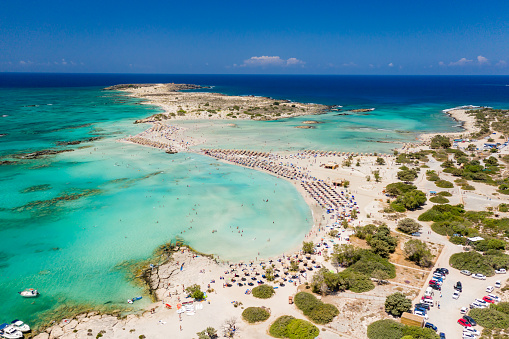 Aerial view of shallow sandy lagoons and a beach surrounded by deeper dark blue sea (Elafonissi Beach)