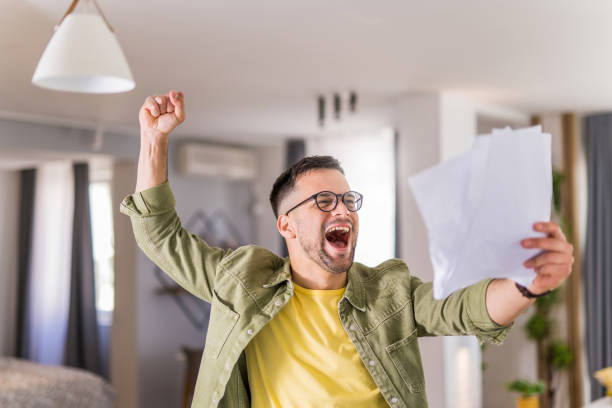 istock Happy young man holding paperwork and celebrating. 1332229845