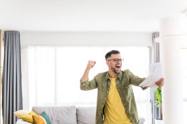 istock Happy young man holding paperwork and celebrating. 1332229865