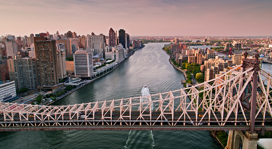 Drone shot of New York City on a summer evening, taken from over the East River, with the Queensboro Bridge spanning between Manhattan and Roosevelt Island.