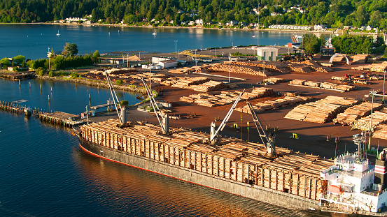Drone shot of the Port of Olympia at the southern end of the Puget Sound in Washington State, where logs are piled up on the dockside and on a boat.