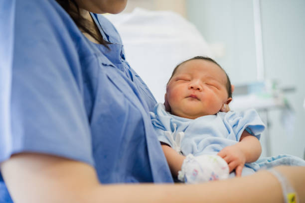 Young mother holding her newborn baby who sleep first days of life at hospital. stock photo